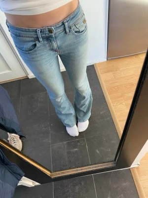 Blå bootcut jeans  - Snygga ljusblå bootcut jeans  med röda kontrastsömmar på bakfickorna och längs midjan. Klassisk femficksmodell med normal passform och lätt slitning på framsidan. Perfekt för dig som gillar retrovibbar och breda ben. 
