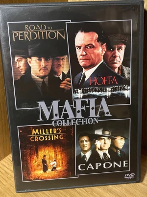 Mafia Collection DVD-box - Säljer en svart DVD-box med fyra klassiska maffiafilmer: Road to Perdition, Hoffa, Miller's Crossing och Capone. Boxen har filmomslag i färg på framsidan och detaljerad info på baksidan. Perfekt för dig som gillar spännande och dramatiska berättelser om gangsters och brott.