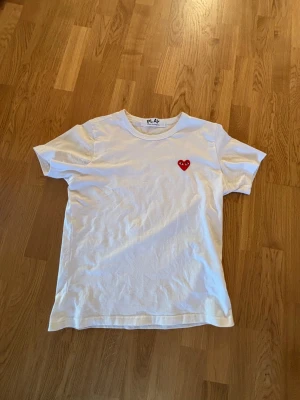 Vit Comme des Garçons PLAY t-shirt - Vit t-shirt från Comme des Garçons PLAY med det ikoniska röda hjärtat med ögon broderat på bröstet. Klassisk rund halsringning och korta ärmar. Tillverkad i mjuk bomull för en skön och avslappnad stil.
