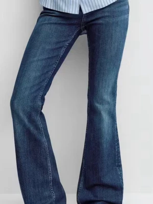 Blå bootcut jeans med hög midja - Snygga blå bootcut jeans med hög midja och klassiska bakfickor. Jeansen har en lätt tvättad look och är tillverkade i denim med stretch för extra komfort. Perfekta för dig som gillar en retroinspirerad stil och vill ha ett par jeans som sticker ut.