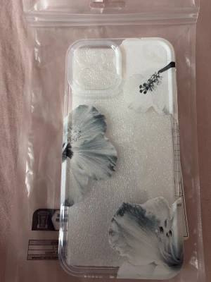 Genomskinligt mobilskal med blommor - Snyggt genomskinligt mobilskal med stora vita och grå blommor. Skalets design är stilren och modern, perfekt för dig som vill ha ett unikt utseende på mobilen. Tillverkat i tålig plast som skyddar din telefon mot repor och stötar. Passar till mobil med större kameralins.