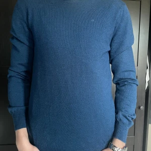 Mörkblå J Lindeberg stickad tröja - Säljer en enkel och stilren snygg mörkblå färg stickad tröja med rund hals och från J Lindeberg. Perfekt för dig som gillar klassiska plagg i garderoben.