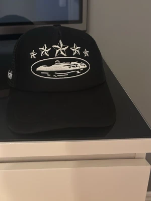 Svart keps från Chimi med brodyr - Cool svart keps från Chimi med vit brodyr framtill som visar fem stjärnor och ett motiv, samt broderad logga bak. Kepsen har mesh-paneler och justerbar snapback. Perfekt för dig som vill ha en unik och trendig accessoar.