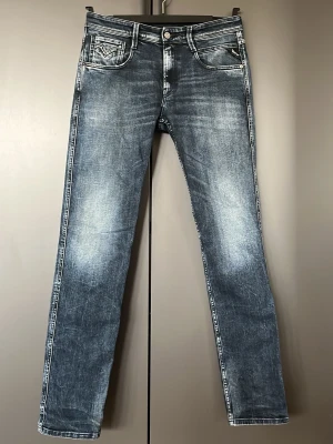 Blå raka jeans från Replay - Snygga blå jeans från Replay med raka ben och slitna detaljer. Jeansen har klassisk femficksmodell, tydliga kontrastsömmar och en tvättad look som ger en cool vintagekänsla. Perfekta för en avslappnad och trendig stil.
