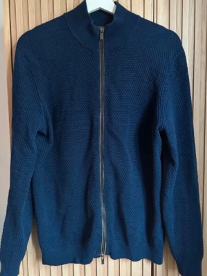 Cardigan Massimo Dutti  - Mörkblå stickad tröja med dragkedja framtill och hög krage. Tröjan har en strukturerad yta och långa ärmar. Perfekt för lager-på-lager och enkel att matcha med jeans eller chinos.