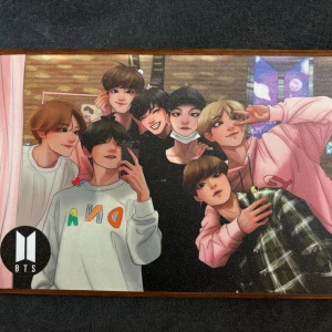 BTS tavla - Säljer en rektangulär tavla med färgglad BTS fanart-motiv, inramad i en ljus träram. Motivet visar flera tecknade personer i olika färgglada kläder och bakgrund med BTS-logga. Baksidan har upphängningsfäste i metall. Perfekt för fans som vill ha något unikt på väggen.