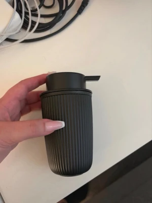 Svart tvålpump i plast - Säljer en stilren svart tvålpump med räfflad yta och modern design. Tillverkad i plast och har ett praktiskt munstycke för enkel dosering av tvål eller lotion. Perfekt för badrum eller kök. Aldrig använt men se bild 2 och 5 för defekt, den behåller dock sin funktion. 
