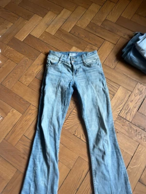 Ljusblå bootcut jeans med pressveck - Säljer ett par ljusblå bootcut jeans med pressveck framtill. Jeansen har klassisk femficksmodell, dubbla knappar i midjan och utsvängda ben. Perfekta för dig som gillar retrostil och vill ha ett par bekväma jeans med snygg passform. Jeansen har en defekt vilket är att vid gylfen saknar själva dragkedja saken, det borde gå jättelätt att sätta till den dock!