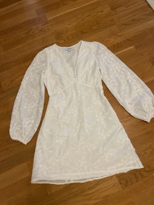  Ny Vit broderad kortklänning Kappahl - Supersöt vit kortklänning från Kappahl med broderade blommor, v-ringning och knappar framtill. Klänningen har långa, lätt puffade ärmar och är gjord i ett tunt, luftigt material som känns perfekt för varmare dagar.
