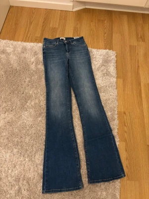 Blå bootcut jeans från ONLY - Snygga blå bootcut jeans från ONLY med klassisk femficksdesign och utsvängda ben. Jeansen har en mellanblå tvätt och är tillverkade i stretchigt denimtyg för extra komfort. Perfekta för en trendig och avslappnad look. Säljer pågrund av att de är för långa. Fint skick men köpte de med slitningar längst ner mot hälen.