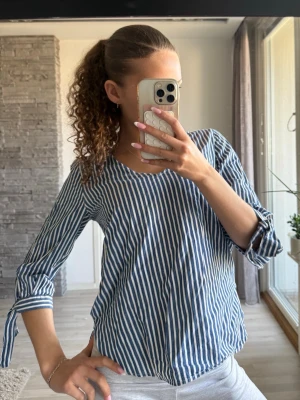 Blåvit randig blus med trekvartsärm - Säljer en blåvit blus med vertikala ränder och v-ringning. Blusen har trekvartsärmar med knytband vid ärmsluten. 💕