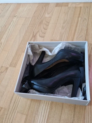 Svarta pumps från Tamaris - Klassiska svarta pumps från Tamaris med rundad tå och bred klack. Skorna är tillverkade i slätt konstläder och har en stilren, tidlös design som passar till många olika outfits. Nypris 699 kr