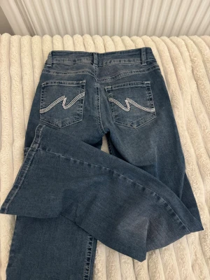 Blå jeans med broderade bakfickor - Snygga blå jeans med raka ben och coola broderade detaljer på bakfickorna. Jeansen har en klassisk femficksmodell och är perfekta för dig som gillar en avslappnad men ändå trendig stil.