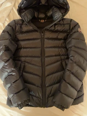 Svart dunjacka från Colmar - Snygg svart dunjacka från Colmar med huva och dragkedja framtill. Jackan har puffig design, och Colmar-logga på ärmen. Perfekt för kalla vinterdagar och riktigt skön att bära. Finns två skador på varav en är laggad. Glömde ta bild men skriv om du vill ha bild på dem.