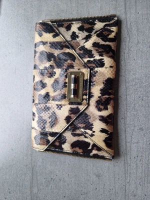 Leopardmönstrad kuvertväska från Diane von fürstenberg  - Snygg kuvertväska från Diane von  fürstenberg i leopardmönstrat konstläder med guldfärgade metalldetaljer. Väskan har ett kuvertformat lock och ett innerfack med dragkedja. Perfekt för dig som vill sticka ut med ett djurmönster.