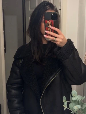 Svart teddyjacka med bred krage - Säljer en svart teddyjacka med bred krage och detaljer i fuskpäls. Jackan har en oversized passform och dragkedja framtill. 