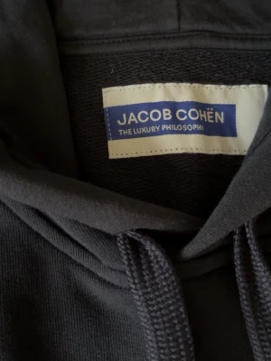 Jacob Cohën Hoodie - Säljer nu denna mörkblå hoodie från Jacob Cohën i storlek M. Den är köpt på butiken Thomas i Halmstad för ungefär ett år sedan. Skicket är 8/10 då den har använts ett flertal gånger under året men några defekter finns inte. Ny pris var 4995kr, pris kan diskuteras.