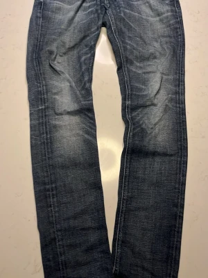 Mörkblåa Nudie Jeans - Säljer ett par mörkblå jeans med raka ben och snygga slitningar på framsidan. Jeansen har klassisk femficksdesign och kontrastsömmar. Perfekta för en avslappnad och trendig look. Materialet är denim i bomull.