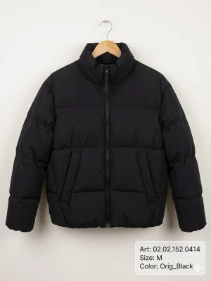 Svart pufferjacka med hög krage - Stilren svart pufferjacka med hög krage och dragkedja framtill. Jackan har en boxig passform och breda kanaler som ger en cool look. Två snedställda fickor på sidorna och elastiska muddar vid ärmsluten. Perfekt för kalla vinterdagar.