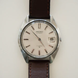 Vintage Seiko | Automatisk - En stilren automatisk klocka Seiko 7005-8000 från 1970-talet med rund silverfärgad boett i rostfritt stål med champagne vit urtavla. Klockan har datumfönster vid kl 3 och klassiskt brunt (after-market) läderband. Perfekt för dig som gillar tidlös design och kvalitet. Klockan är fungerande men har ej servats sedan cirka 2017 i samband med köp.