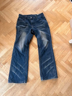 Blå bootcut jeans med slitningar - Säljer ett par blå bootcut jeans med tydliga slitningar och ljusa partier på lår och knän. Jeansen har fem fickor, broderad detalj på ena bakfickan och klassisk knappgylf. Perfekta för en avslappnad och trendig look. Fråga om mått! 💝