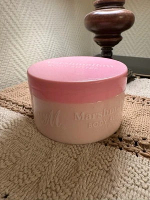 Marshmallow Body Butter rosa burk - Oanvänd! Söt body butter från Barry M i en rund burk med rosa lock och ljusrosa kropp. Doften är marshmallow och burken har en mjuk, feminin design. Perfekt för dig som vill ha en återfuktande och väldoftande hudvård.