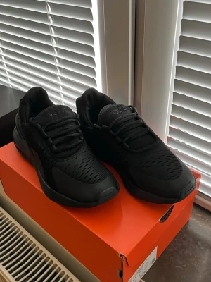 Svarta Nike Air Max 270 sneakers - Snygga helsvarta Nike Air Max 270 sneakers med mesh- och syntetmaterial. Skorna har en chunky sula med synlig Air-enhet i hälen Perfekta för dig som gillar sportig och modern stil.