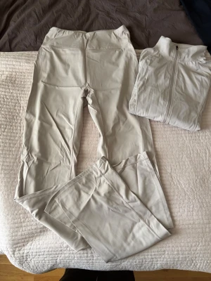 Beige träningsset med ziptröja - Snyggt beige träningsset med ett par utsvängda träningsbyxor och en matchande ziptröja. Tillverkade i mjukt och stretchigt material som passar perfekt för gymmet eller yoga. Byxorna passar på mig som är 175 