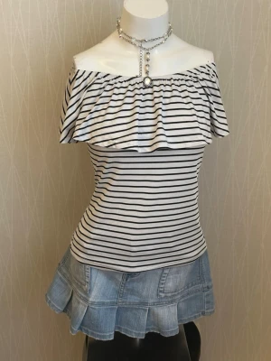 Randig offshoulder topp med volang - Snygg offshoulder topp med svartvita ränder och bred volang runt axlarna. Toppen är figurnära och har en fräsch, somrig känsla. Perfekt att matcha med jeans eller kjol för en trendig look.