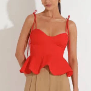 Röd topp med knytband - Trendig röd topp med peplumvolang och smala axelband som knyts på axlarna. Snygg sweetheart-urringning och figurnära passform upptill. Perfekt för dig som vill ha en färgstark och feminin look.