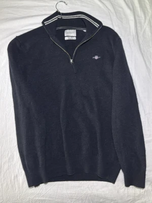 Marinblå halvzip tröja från GANT - Snygg marinblå tröja från GANT med halvzip och ståkrage. Tröjan har diskret logga broderad på bröstet och vita detaljer på kragen. sopass klassisk och enkel att matcha till olika outfits. Perfekt för dig som gillar stilrena plagg. Men är lite liten i storleken så ni vet.