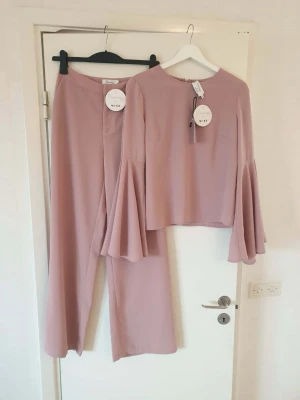 Byxor & topp - Ljusrosa set med vida byxor och matchande topp med trumpet ärmar från NA-KD. Storlek 36 på båda. 