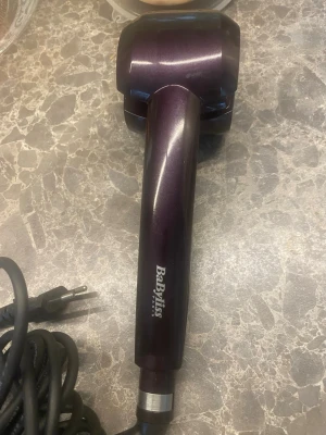 BaByliss Curl Secret locktång - Säljer en mörklila BaByliss Curl Secret locktång med automatisk lockfunktion. Verktyget har en sladd med stickkontakt, tydliga reglage på sidan och är tillverkat i plast och metall. Perfekt för att fixa snygga lockar snabbt och enkelt.