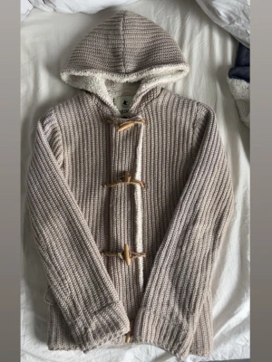 Unik fodrad cardigan - Mysig beige stickad jacka med huva och träknappar. Insidan är fodrad med mjuk fleece för extra värme (en av de skönaste plaggen jag har haft på mig). Perfekt för kyliga dagar. Märket är tokyo branding typ och den är väldigt svår att få tag på nypriset är runt 1500kr.  Ifall mer frågor eller bilder var inte rädda att skriva! Mvh