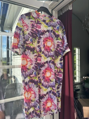 Flerfärgad tie-dye t-shirt-klänning.  - Säljer en färgstark tie-dye t-shirt-klänning från Monki. med korta ärmar. T-shirten-klänningen har ett stort mönster i lila, rosa, cerise, gult och vitt. Tillverkad i mjuk bomull och har en oversize  passform härlig att bara slänga på. 