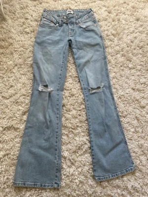 Ljusblå bootcut jeans från 157 - Säljer ett par ljusblå bootcut jeans från 157 i storlek XS. Jeansen har slitna detaljer vid knäna och klassisk femficksdesign. Tillverkade i denim med full längd och snyggt utsvängda ben. Perfekta för en avslappnad och trendig look.