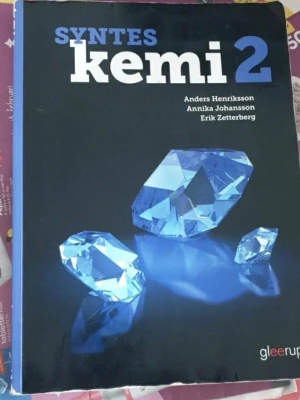 Syntes Kemi 2 kursbok - Kurslitteratur i kemi för gymnasiet, Syntes Kemi 2. Boken har svart omslag med blå och vita diamanter på framsidan. Författare är Anders Henriksson, Annika Johansson och Erik Zetterberg. Perfekt för dig som läser Kemi 2.