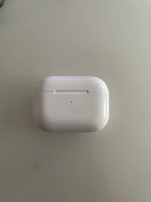 Hörlurar - Säljer ett par Apple AirPods Pro med trådlöst laddningsetui. Hörlurarna är vita, har en stilren och kompakt design och är tillverkade i blank plast. Perfekta för dig som vill ha brusreducering och smidig anslutning till iPhone eller andra Apple-enheter.