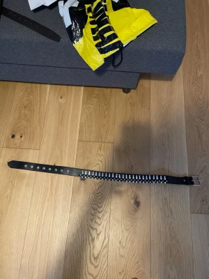 Svart bälte med nitar och silverdetaljer - Snyggt svart bälte med silverfärgade nitar längs hela bandet och ett klassiskt spänne i silver. Perfekt accessoar för att ge din outfit en edgy vibe. Bältet är ca 92 cm långt och har flera hål för justerbar passform.