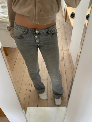 Grå raka jeans - Säljer ett par grå jeans med raka ben. Jeansen har tre synliga knappar framtill och klassisk femficksdesign. Perfekta för en avslappnad och trendig look. Storlek 152