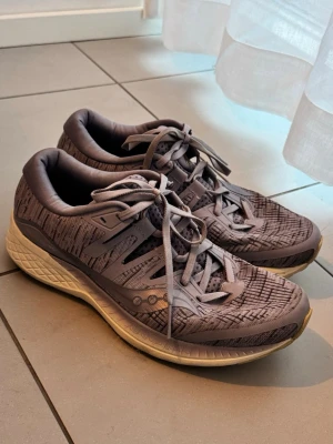 Oanvända Saucony sneakers  - Snygga oanvända sneakers från Saucony med diskret mönster på ovandelen och klassisk logga på sidan. Skorna har en tjock, vit sula med bra dämpning och grå snörning. Ovandelen är i mesh och syntetmaterial för bra andningsförmåga. Storlek 40 nypris runt 2000