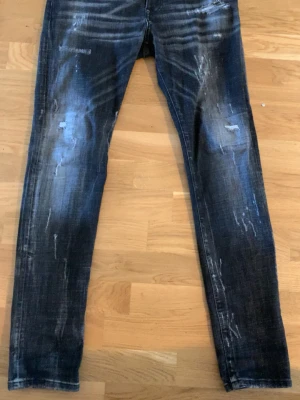 Dsq2 jeans  - Säljer ett par mörkgrå jeans med slitningar och distressed detaljer framtill. Jeansen har en tvättad look med ljusare partier och smal passform. Perfekta för en trendig och avslappnad stil.