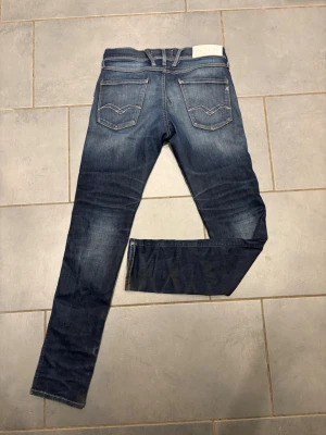Blå jeans från Replay med kontrastsömmar - Snygga blå jeans från Replay med klassisk femficksmodell och ljusa kontrastsömmar. Bakfickorna har coola broderade detaljer och tvätten ger en avslappnad vibe. Perfekta för dig som gillar en tidlös men trendig look. Model: replay hyperflex anbass