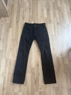Svarta raka jeans från Levi's 501 - Säljer ett par svarta jeans från Levi's med klassisk rak passform och fem fickor. Jeansen har en läderpatch bak i midjan och är tillverkade i ett slitstarkt bomullstyg. Perfekta för dig som gillar en tidlös och clean look. Storlek W31 L34