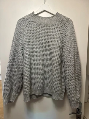 Grå stickad tröja  - Säljer en grå stickad tröja med ett snyggt strukturmönster och rund hals. Tröjan har långa ärmar och ribbade muddar vid ärmslut och nederkant. Perfekt för lager på lager och riktigt mysig till kyliga dagar.