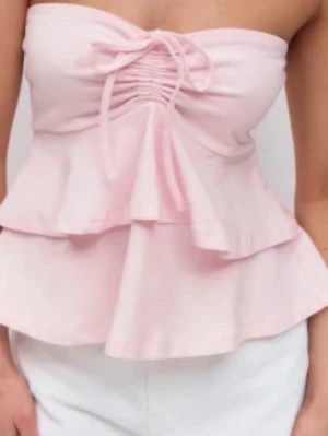Ljusrosa bandeau topp med volanger - Supersöt ljusrosa bandeau topp slutsåld från Gina trixig  med volangdetaljer och snörning framtill. Toppen är axelbandslös och har en feminin, flowy passform som ger en romantisk vibe. Perfekt för varma dagar och somriga outfits.