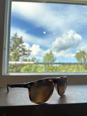 Bruna solglasögon från Ray-Ban - Snygga solglasögon från Ray-Ban med klassisk brunmelerad båge och bruna glas. Modellen har en tidlös, rektangulär form och Ray-Ban-loggan syns på linsen. Perfekta för soliga dagar och ger en cool vibe till din outfit.