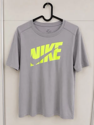 Grå Nike Dri-Fit t-shirt XL - Säljer en grå Nike Dri-Fit t-shirt i storlek XL med stort neongult Nike-tryck på bröstet. T-shirten är tillverkad i ett funktionsmaterial som andas och har en klassisk passform med korta ärmar och rund hals. Perfekt för dig som gillar sportig stil. Står storlek XL som storlek men passform är M/S.