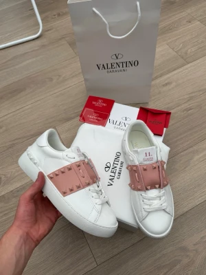 Valentino Garavani vita sneakers - Säljer mina Valentino Garavani Rockstud Untitled sneakers i vitt läder med rosa detaljer och ikoniska nitar. Stilrena och exklusiva skor som passar till alla tillfällen. Säljs med originalkartong, dustbag, påse och tillhörande kort enligt bilderna. Mycket fint skick. Hör gärna av er vid frågor! 