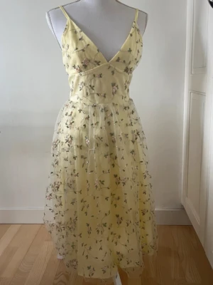 Gul blommig klänning med broderi - storlek 36/S        köpt för 400kr aldrig använt , pruta ner priset går kanske med på det ;)                                                   Söt gul klänning med tunna axelband och v-ringning. Klänningen har ett lager av transparent tyg med broderade blommor i rosa och grönt, vilket ger en romantisk känsla. Perfekt för sommarens alla tillfällen!